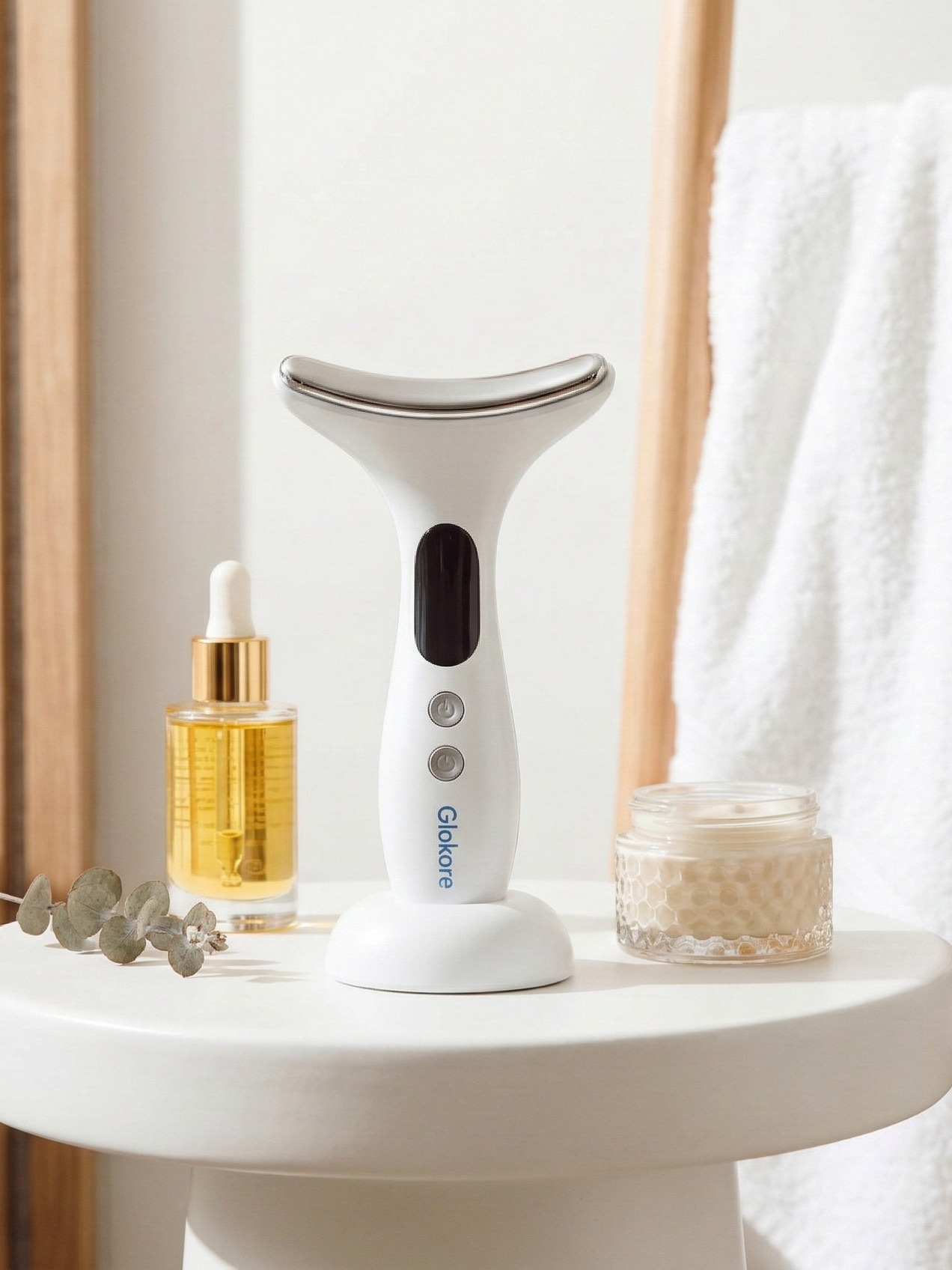 The Glokore Facial Sculptor sits perfectly centered on a matte black background with a single spotlight above it, creating a dramatic skincare product moment with soft shadows and cinematic lighting.